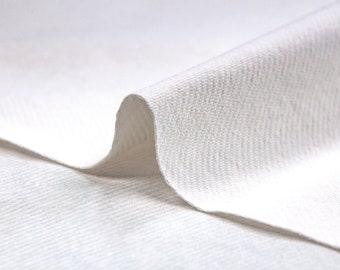 May include: Close-up of a white fabric with a textured surface. The fabric is folded over itself, creating a soft, curved shape.