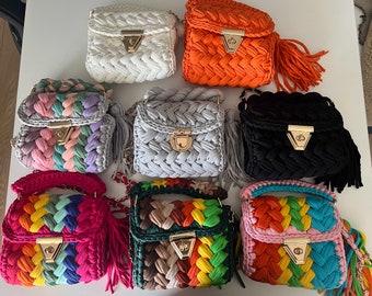 May include: A collection of handmade, small, braided-style handbags in various colors. The bags feature a flap closure with a gold-colored clasp and a matching chain strap. Some bags have a tassel. Colors include white, orange, black, gray, and rainbow.