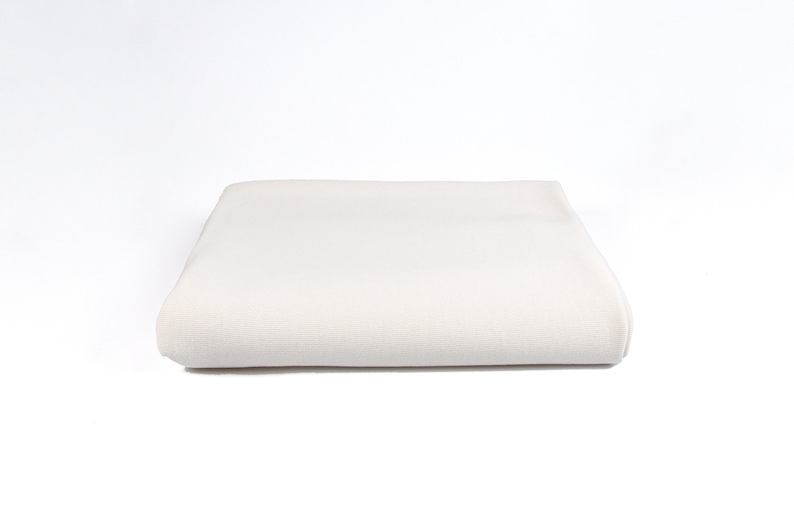 May include: A folded white cotton fabric, possibly a sheet or tablecloth, with a smooth texture.