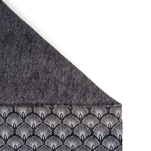 May include: A black and white patterned fabric with a gray fleece lining. The fabric features a repeating design of stylized white fans on a black background.