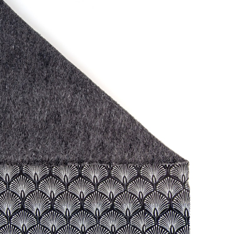 May include: A black and white patterned fabric with a gray fleece lining. The fabric features a repeating design of stylized white fans on a black background.