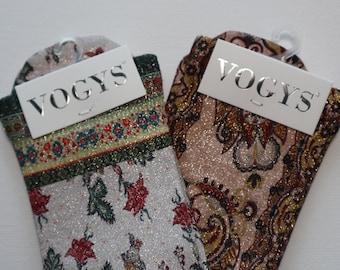 Può includere: Due paia di calzini con finitura glitterata. Un paio ha un motivo floreale in tonalità di rosso, verde e oro su sfondo bianco. L'altro paio ha un motivo paisley in tonalità di marrone, rosso e oro su sfondo rosa. Entrambi i paia hanno un'etichetta bianca con la parola "VOGYS" stampata su di essi.