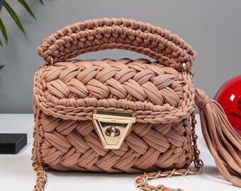 May include: A small, woven handbag with a gold chain strap and a tassel. The bag is a light brown color and has a gold clasp.