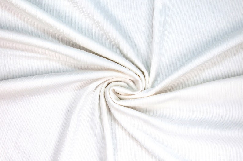 May include: White ribbed fabric with a soft, smooth texture. The fabric is folded and twisted, creating a swirling pattern.