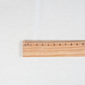 May include: A wooden ruler with black markings for centimeters and inches. The ruler is 15 centimeters long and has markings from 0 to 15.