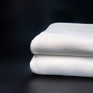 May include: Two white cotton fabric sheets stacked on top of each other against a black background.