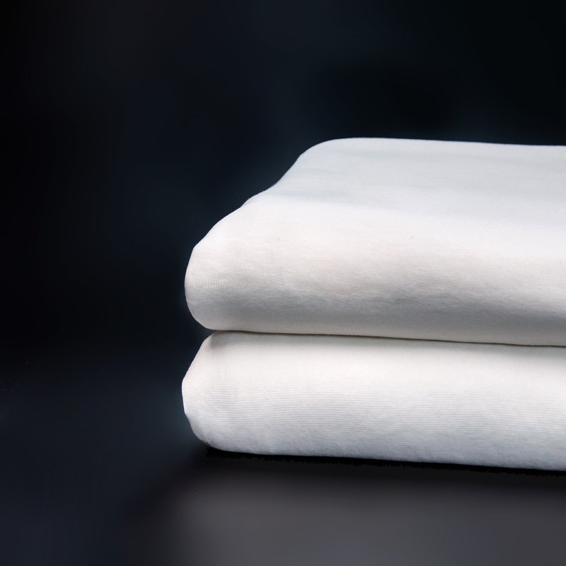 May include: Two white cotton fabric sheets stacked on top of each other against a black background.