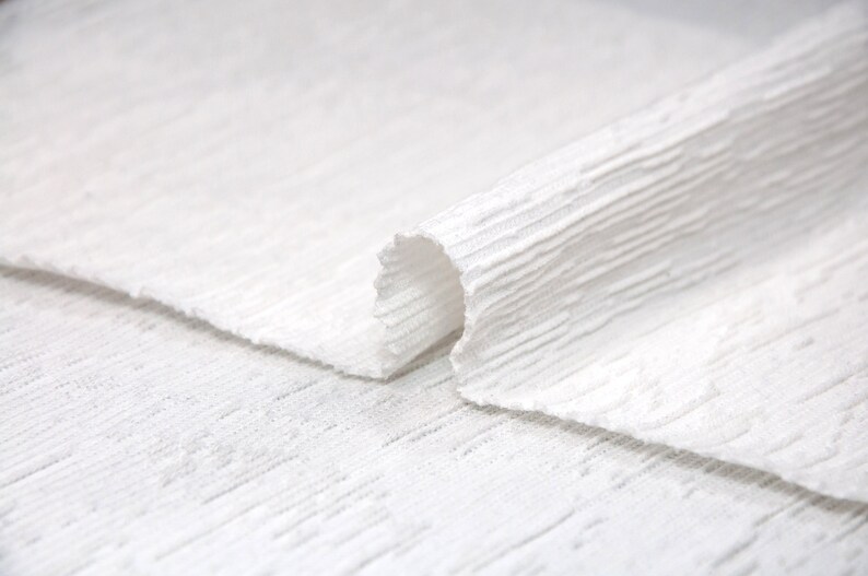 May include: White textured fabric folded over itself, showing the texture of the fabric.