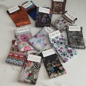 Può includere: Una collezione di calzini fantasia con il marchio "VOGYS" su ogni etichetta. I calzini presentano vari disegni, tra cui floreali, animalier e astratti. I colori includono sfumature di marrone, blu, rosa e verde. Ogni paio è piegato e presentato con un gancio.