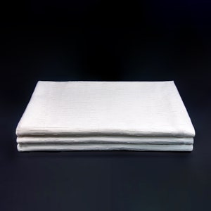 May include: A stack of three white linen napkins folded neatly on a black surface.