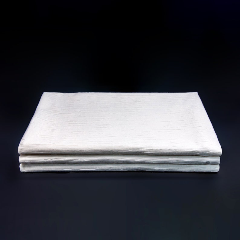 May include: A stack of three white linen napkins folded neatly on a black surface.