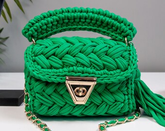 May include: A small green crocheted handbag with a gold chain strap and a gold clasp. The bag has a tassel on the side.