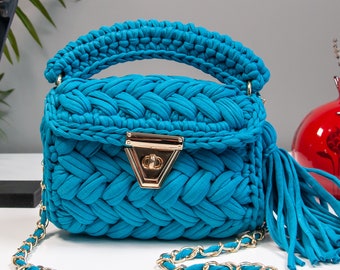 May include: A small, bright blue crocheted handbag with a gold chain strap and a gold clasp. The bag has a tassel on the side.
