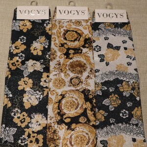 May include: Three pairs of socks with the brand name "VOCYS" at the top. The socks feature various patterns, including floral and ornate designs in black, gold, and white. The socks have a shiny, glittery appearance.