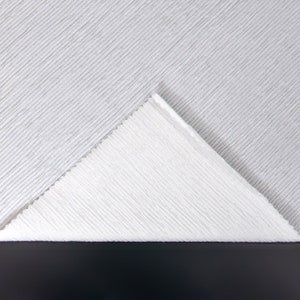 May include: Close-up of two white ribbed fabrics, one folded over the other, creating a triangular shape. The fabric has a subtle texture and a soft, light appearance.
