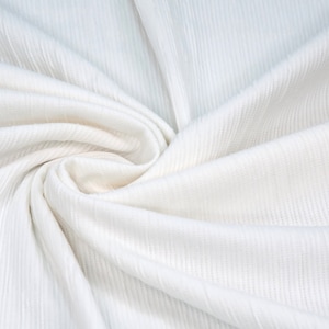 May include: White ribbed fabric with a soft, smooth texture. The fabric is folded and draped, showcasing its texture and drape.
