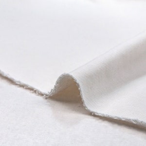 May include: Close-up of a white ribbed fabric with a slightly frayed edge. The fabric is soft and smooth, with a subtle texture.