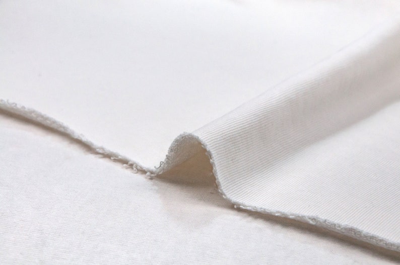 May include: Close-up of a white ribbed fabric with a slightly frayed edge. The fabric is soft and smooth, with a subtle texture.