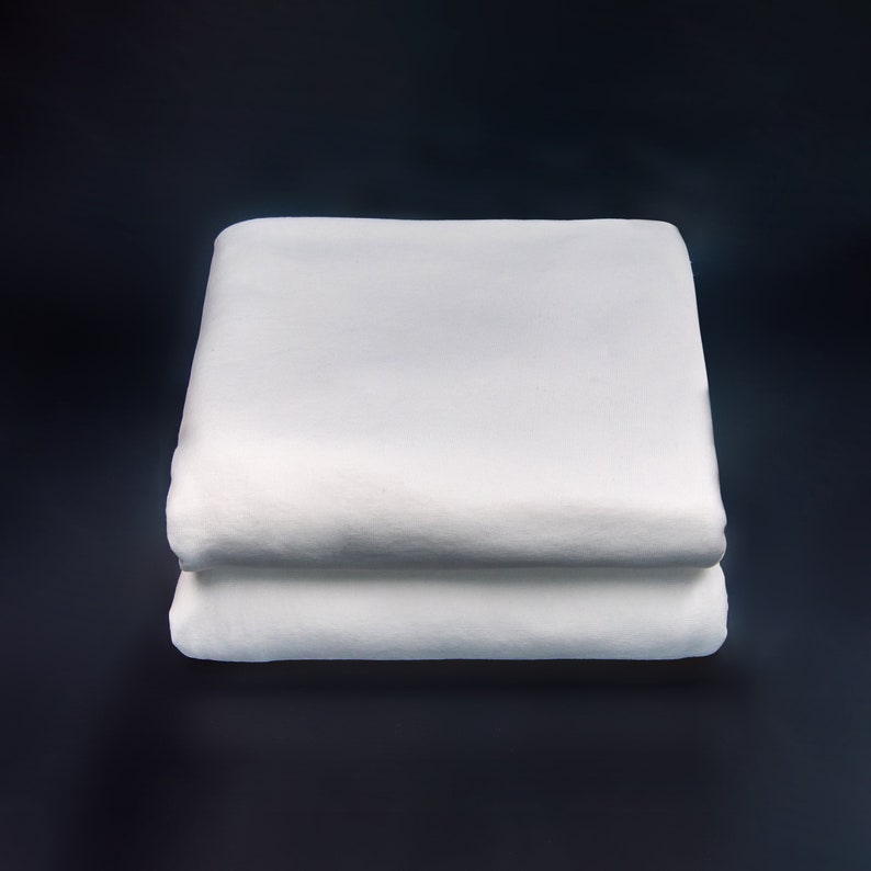 May include: Two white folded fitted sheets, one on top of the other, against a dark background.