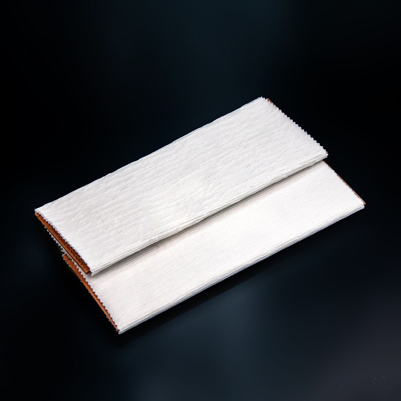 May include: Two white tissue paper sheets folded in half, with the edges of the paper slightly overlapping. The paper has a subtle texture and is folded in a way that creates a rectangular shape.