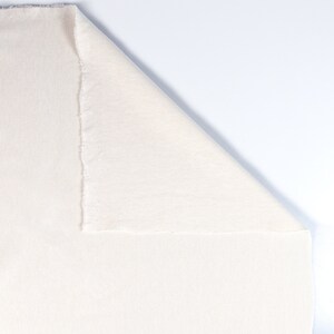 May include: A close-up of a white fabric with a ribbed texture. The fabric is folded in half, with one side folded over the other.