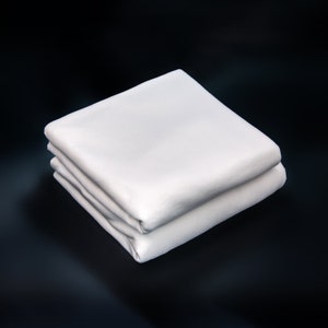 May include: A white cotton fitted sheet folded in half, showing the smooth texture of the fabric.