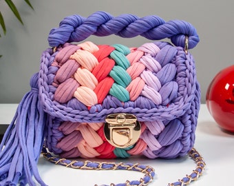 May include: A multi-colored crocheted handbag with a gold chain strap and a gold clasp. The bag has a purple tassel and is made of a soft, textured fabric.