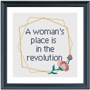 May include: A cross-stitch pattern with a gold geometric frame and a pink flower. The text inside the frame reads "A woman's place is in the revolution."