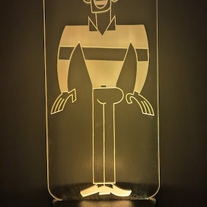 May include: A white acrylic night light with a cartoon character design. The character is a person with a striped shirt and a smile. The night light has a black base with an on/off switch.