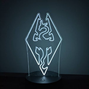 May include: A white illuminated night light shaped like the dragon symbol from the video game The Elder Scrolls V: Skyrim.