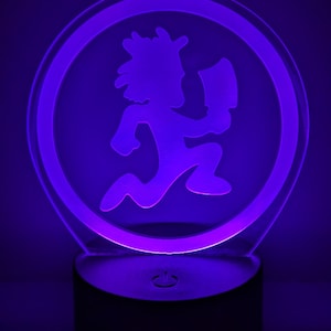 May include: A purple LED night light with a clear acrylic base and a circular design featuring a running figure with an axe. The figure is in a circle with a white outline.