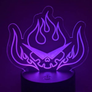 May include: A purple night light shaped like a skull with flames. The skull has a stylized design with a pointed nose and a single eye. The flames are stylized and have a pointed shape.