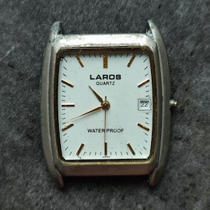 May include: A silver-toned wristwatch with a white face and gold accents. The watch face features the text "LAROS QUARTZ" and "WATER PROOF" along with a date window displaying the number "22".