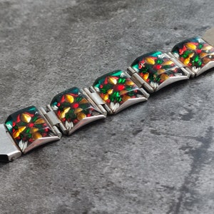 May include: A silver bracelet with a series of square-shaped, colorful glass tiles. Each tile features a floral design with red, green, yellow, and white accents.