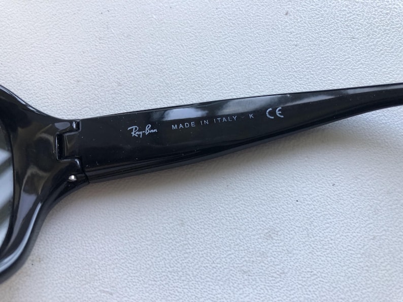 May include: Close-up of a black Ray-Ban sunglasses arm. The text "Ray-Ban" is visible, along with "MADE IN ITALY" and "CE". The sunglasses arm is glossy black.