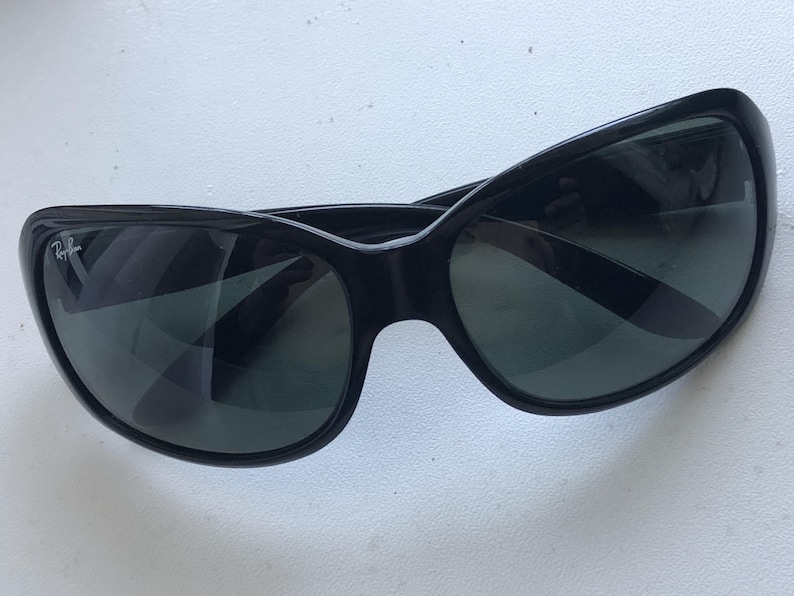 May include: Black sunglasses with a curved frame and dark lenses. The sunglasses have a glossy finish and a small logo on the left side. The lenses are reflective, and the overall design is sleek and modern.