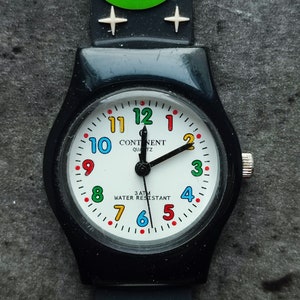 May include: Black wristwatch with a white face and colorful numbers. The watch has a black band with a green and white design.
