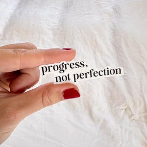May include: White sticker with black text that reads "progress, not perfection".