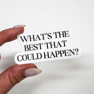 May include: A white sticker with the text "WHAT'S THE BEST THAT COULD HAPPEN?" in black, held by a hand. The sticker has a unique, irregular shape. The background is plain white.
