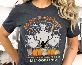 May include: A dark grey heather t-shirt with a graphic of a ghost chef with a rolling pin and whisk, surrounded by three ghosts and pumpkins. The text "BOOO-N APPETIT!" is above the graphic and "SERVING UP TREATS FOR OUR LIL' GOBLINS!" is below the graphic.