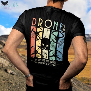 May include: Black t-shirt with a vintage-style graphic of a drone with a skull in the center. The text "Drone Pilot" is above the graphic and "In Drone We Trust In Batteries We Pray" is below.
