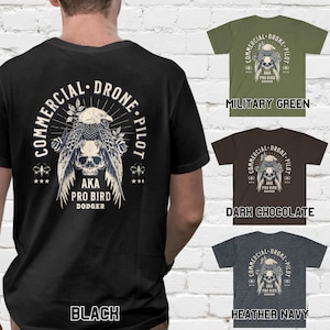 May include: Black, military green, dark chocolate, and heather navy t-shirts with a graphic print of a skull with wings and the text "Commercial Drone Pilot AKA Pro Bird Dodger".