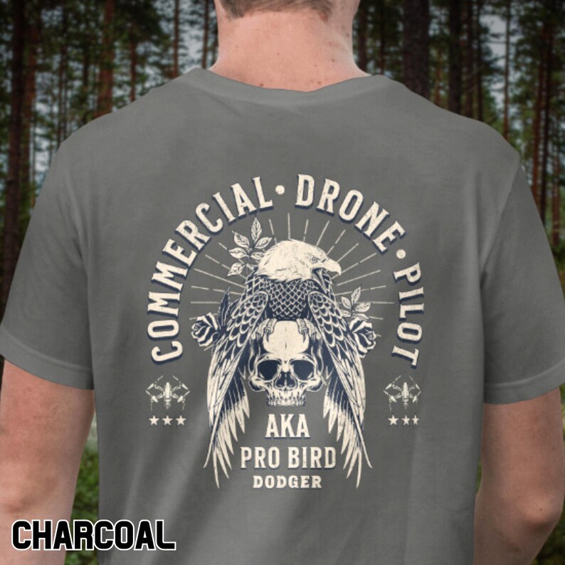 May include: A charcoal grey t-shirt with a vintage-style graphic of an eagle perched on a skull. The graphic includes the text "Commercial Drone Pilot", "AKA", "Pro Bird", and "Dodger".