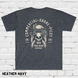 May include: Heather navy blue t-shirt with a graphic of a skull with wings and the text "Commercial Drone Pilot AKA Pro Bird Dodger".