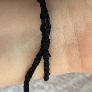 May include: A black braided cord bracelet on a person's wrist.