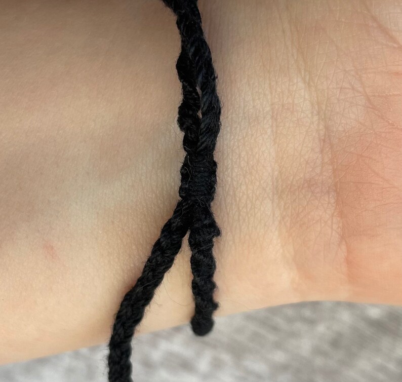 May include: A black braided cord bracelet on a person's wrist.