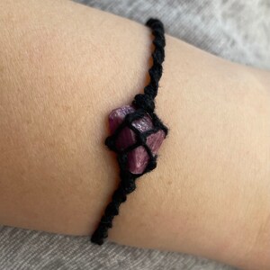 May include: A black cord bracelet with a purple crystal wrapped in the cord.