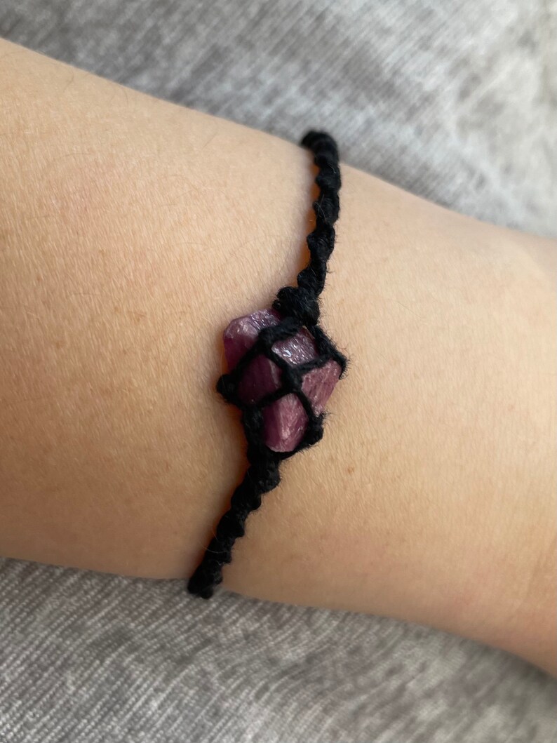 May include: A black cord bracelet with a purple crystal wrapped in the cord.