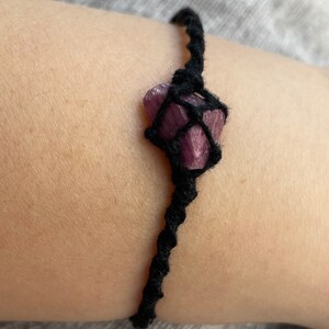 May include: A black cord bracelet with a purple crystal wrapped in the cord.