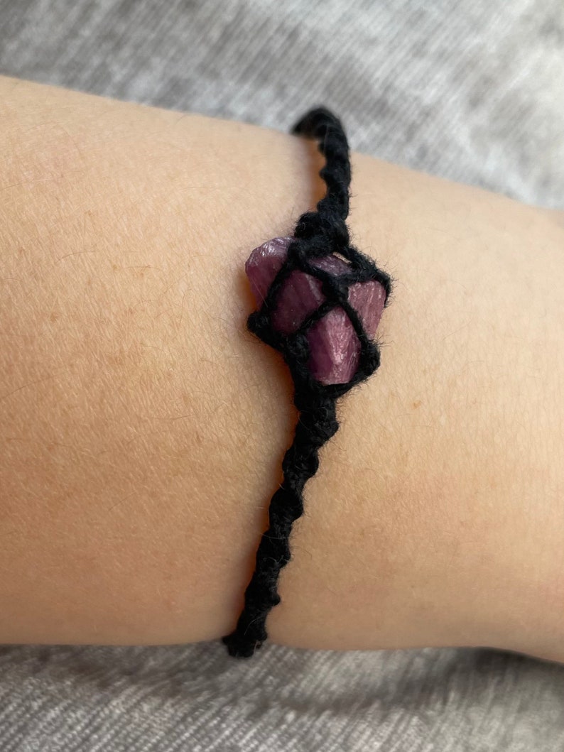 May include: A black cord bracelet with a purple crystal wrapped in the cord.